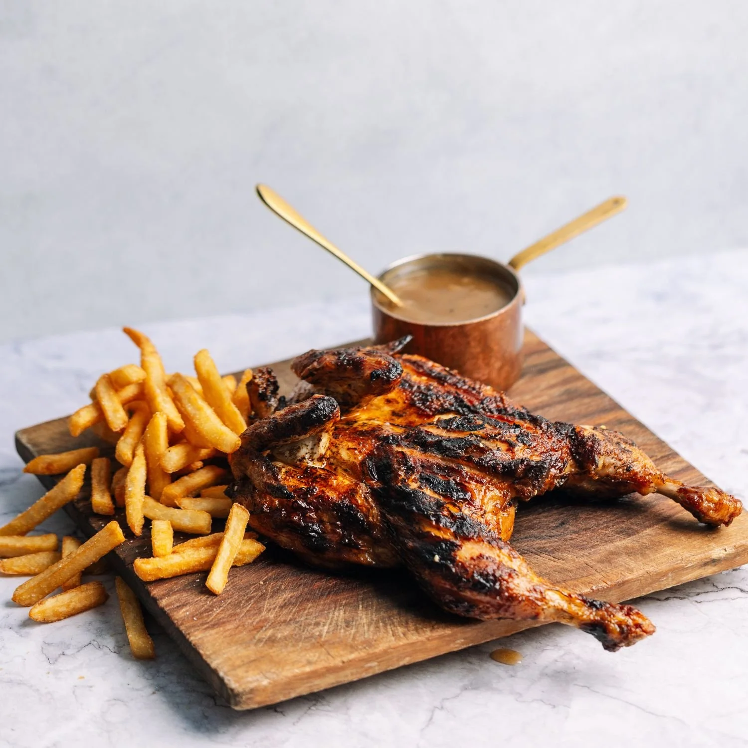Charcoal grilled chicken with hot chips and gravy on a wooden board